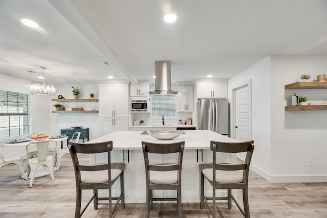 kitchen featuring a kitchen breakfast bar, appliances with stainless steel finishes, light hardwood / wood-style floors, white cabinetry, and island exhaust hood