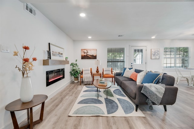 living area with visible vents, a glass covered fireplace, light wood-style flooring, and recessed lighting