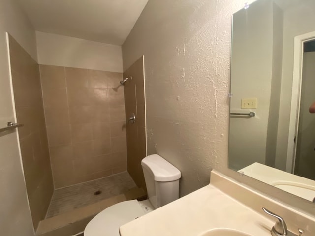 bathroom with toilet, a tile shower, and vanity