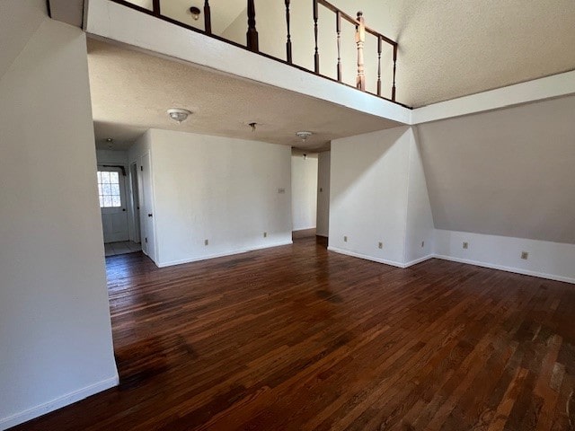 unfurnished living room featuring a textured ceiling, lofted ceiling, and dark wood-type flooring