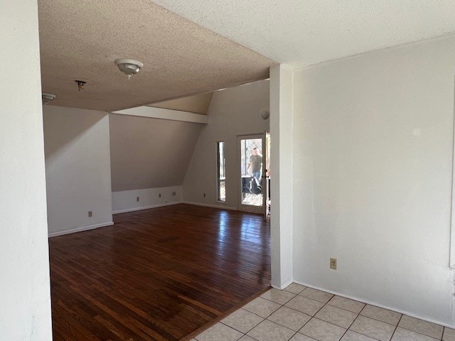 unfurnished room featuring light tile patterned flooring, lofted ceiling, and a textured ceiling