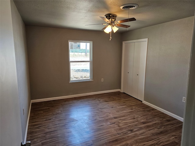 unfurnished bedroom with baseboards, visible vents, dark wood-style floors, a textured ceiling, and a closet