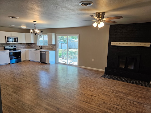 unfurnished living room with sink, brick wall, a fireplace, ceiling fan with notable chandelier, and dark hardwood / wood-style flooring