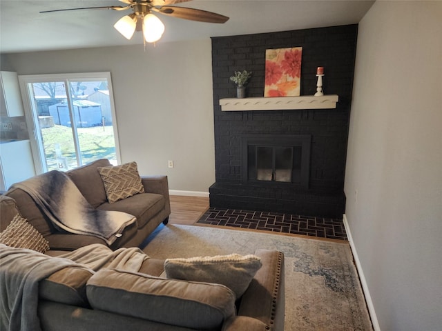 living area with a ceiling fan, a fireplace, baseboards, and wood finished floors