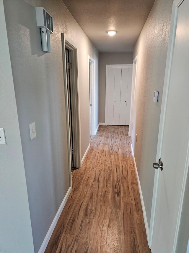 hallway with light wood-type flooring, baseboards, a textured ceiling, and a textured wall