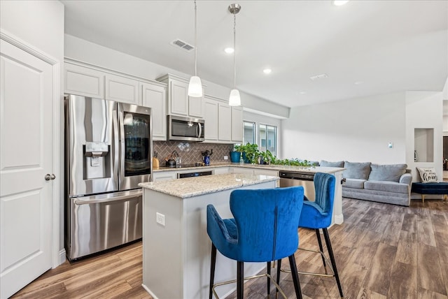 kitchen with tasteful backsplash, appliances with stainless steel finishes, light stone counters, hardwood / wood-style flooring, and decorative light fixtures