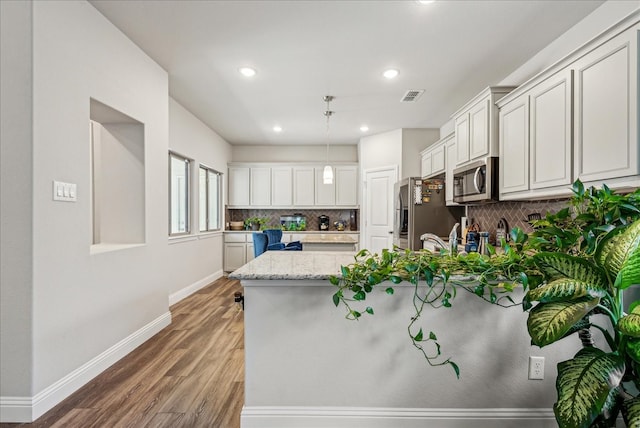 kitchen with tasteful backsplash, light hardwood / wood-style floors, light stone counters, and appliances with stainless steel finishes