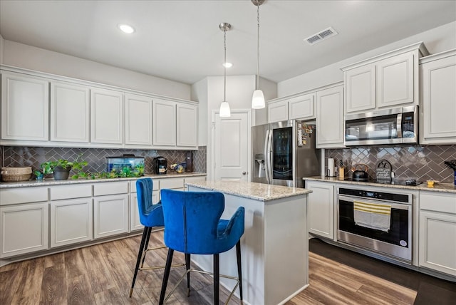 kitchen featuring hardwood / wood-style floors, appliances with stainless steel finishes, tasteful backsplash, and white cabinetry