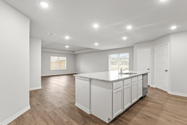 kitchen with light stone counters, a center island with sink, dark hardwood / wood-style flooring, dishwasher, and white cabinets