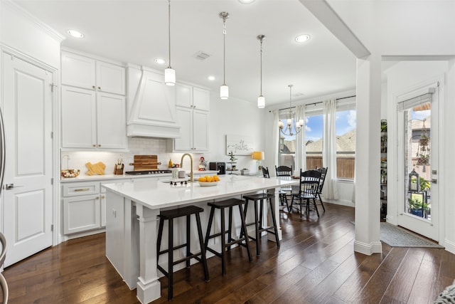 kitchen with premium range hood, an island with sink, white cabinets, dark hardwood / wood-style flooring, and hanging light fixtures