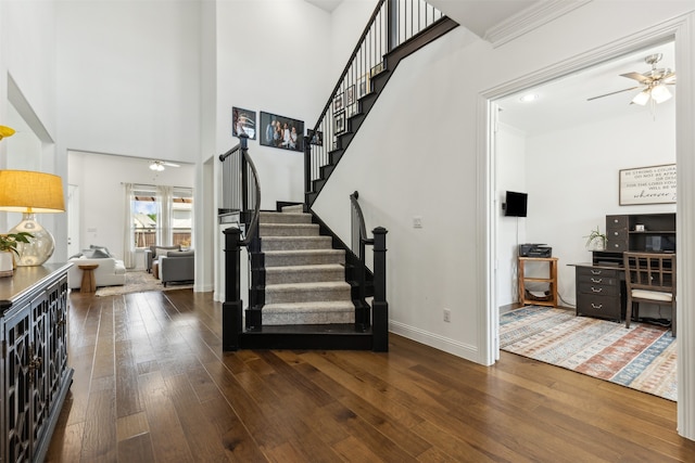 staircase with ceiling fan, a towering ceiling, and wood-type flooring