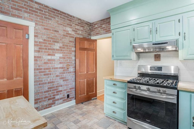 kitchen with stainless steel gas stove, light tile patterned flooring, butcher block countertops, and brick wall