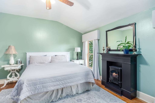 bedroom featuring ceiling fan, vaulted ceiling, a wood stove, and wood-type flooring