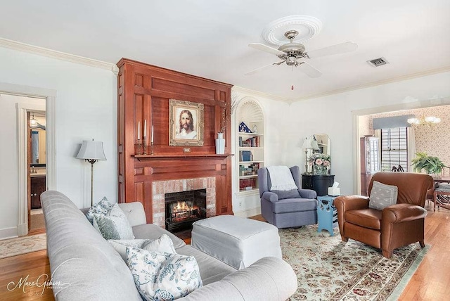 living room with hardwood / wood-style floors, ornamental molding, built in shelves, a fireplace, and ceiling fan