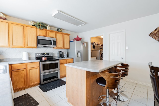 kitchen featuring light tile patterned flooring, backsplash, a center island, appliances with stainless steel finishes, and independent washer and dryer