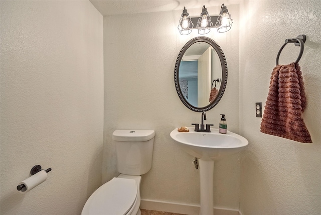 half bathroom with a textured wall, a sink, and toilet