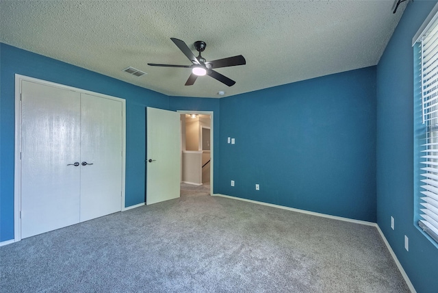 unfurnished bedroom featuring visible vents, ceiling fan, a textured ceiling, carpet flooring, and a closet