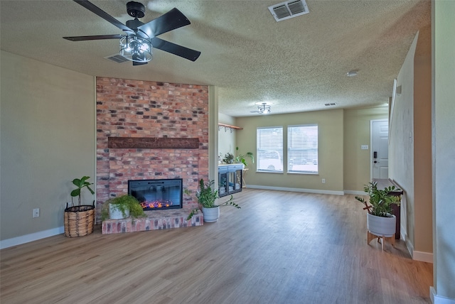 living room with a textured ceiling, a brick fireplace, wood-type flooring, and ceiling fan