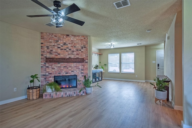 living area with visible vents, a brick fireplace, wood finished floors, and a ceiling fan