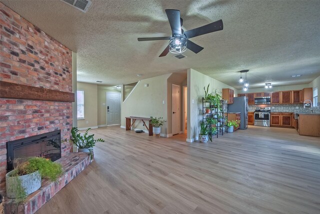 unfurnished living room featuring baseboards, visible vents, light wood-style flooring, a textured ceiling, and a fireplace