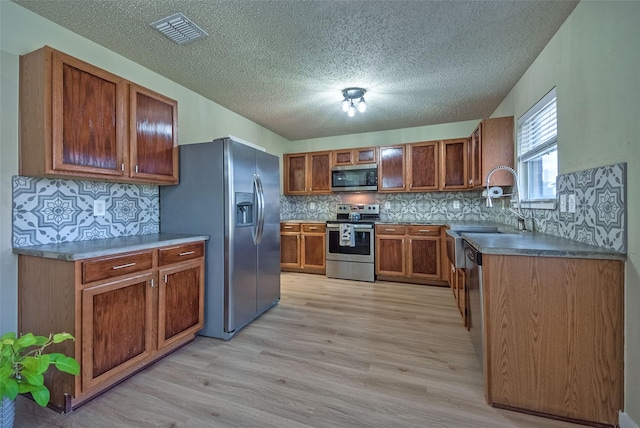 kitchen featuring visible vents, appliances with stainless steel finishes, light wood-type flooring, tasteful backsplash, and brown cabinetry