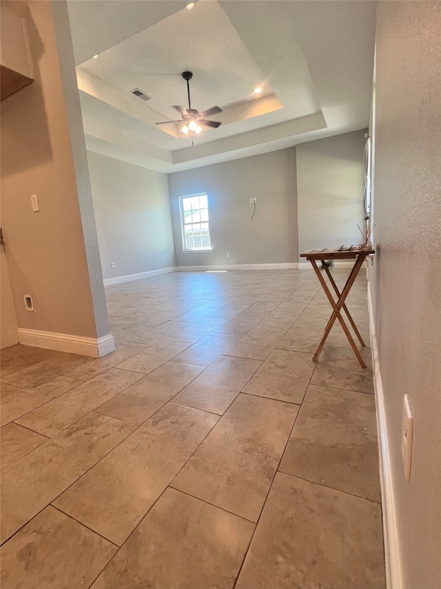 empty room featuring ceiling fan with notable chandelier and a raised ceiling