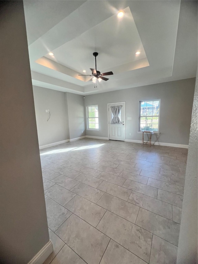 unfurnished room featuring ceiling fan, a healthy amount of sunlight, and a raised ceiling