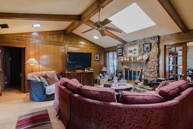 living room featuring vaulted ceiling with beams, light wood-type flooring, wood walls, and a stone fireplace