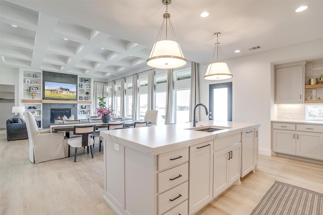 kitchen featuring hanging light fixtures, a kitchen island with sink, white cabinetry, beamed ceiling, and sink