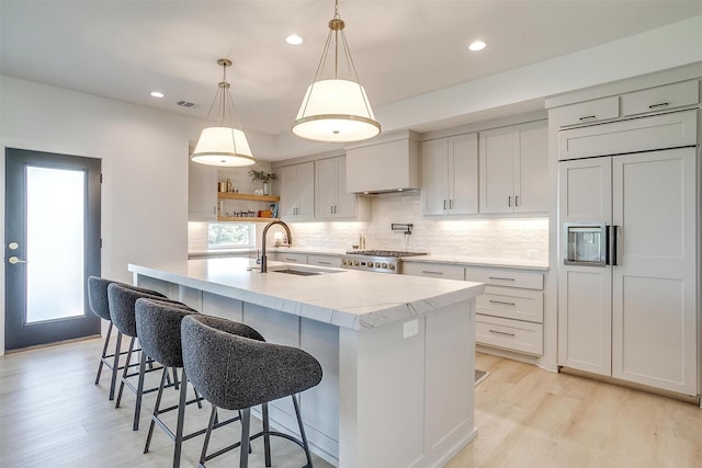 kitchen with visible vents, paneled refrigerator, light wood-type flooring, a sink, and tasteful backsplash