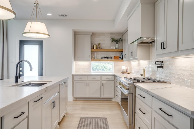 kitchen featuring light stone countertops, custom exhaust hood, pendant lighting, high end stainless steel range, and sink