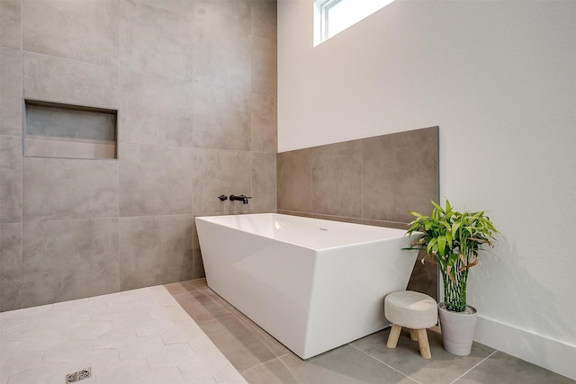 full bathroom with tile patterned floors, a freestanding bath, and tile walls