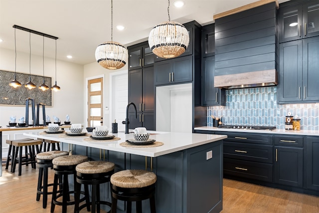 kitchen with hanging light fixtures, a center island with sink, stainless steel gas stovetop, and light hardwood / wood-style flooring