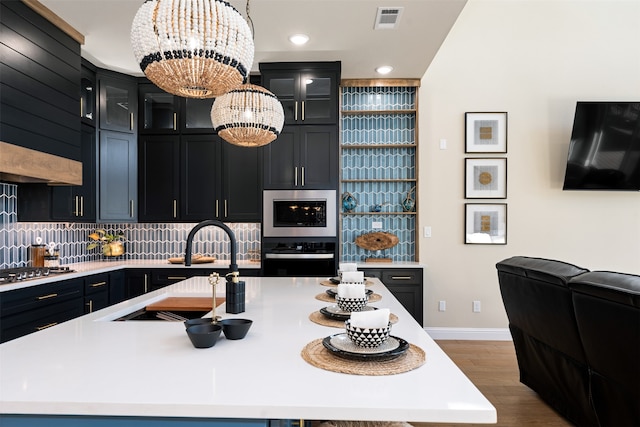 kitchen featuring tasteful backsplash, appliances with stainless steel finishes, pendant lighting, sink, and an island with sink