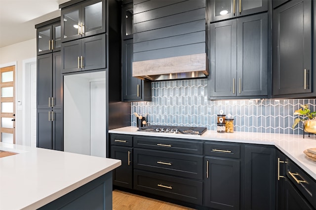 kitchen with light wood-type flooring, stainless steel gas cooktop, decorative backsplash, and premium range hood