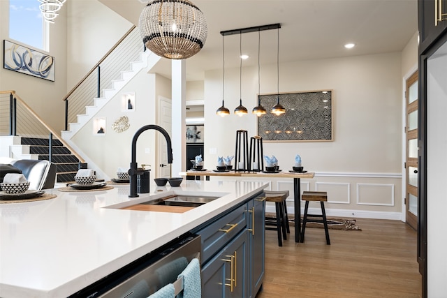 kitchen with decorative light fixtures, an inviting chandelier, sink, light hardwood / wood-style floors, and stainless steel dishwasher