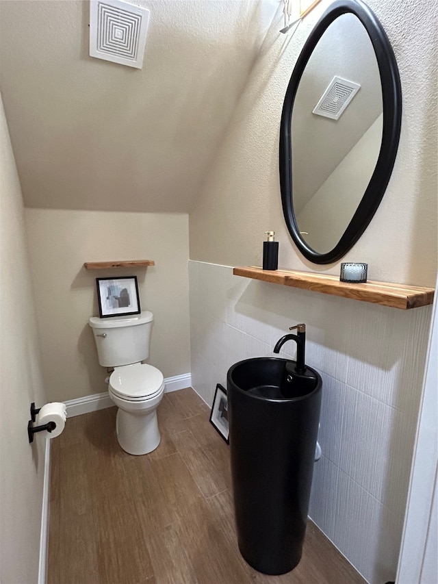 bathroom featuring tile walls, wood-type flooring, and vaulted ceiling