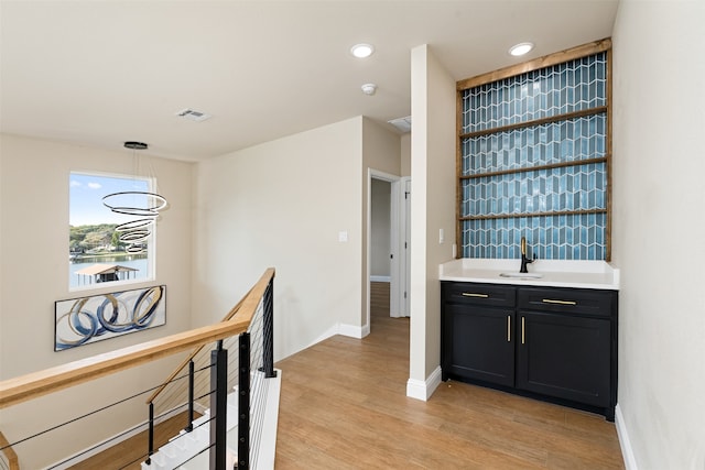 bar with an inviting chandelier, light wood-type flooring, pendant lighting, and sink