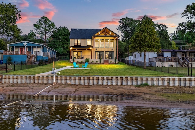 back house at dusk with a water view, a yard, and a balcony