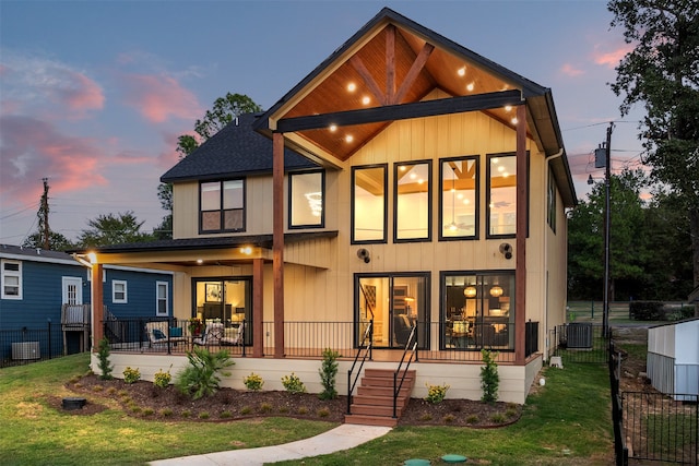 back house at dusk featuring central AC unit, a lawn, and a porch