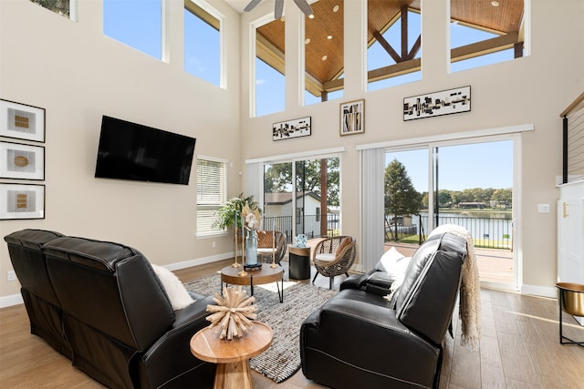 living room with a high ceiling, light wood-type flooring, a water view, and ceiling fan