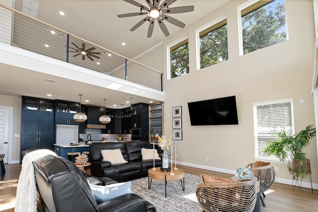 living room with a high ceiling, sink, ceiling fan, and light hardwood / wood-style flooring