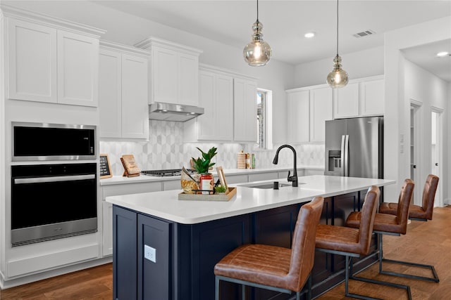 kitchen featuring range hood, sink, white cabinets, a kitchen island with sink, and stainless steel appliances