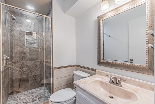 bathroom with tile walls, toilet, vanity, and an enclosed shower