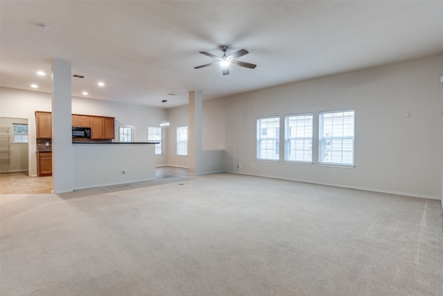 unfurnished living room with light colored carpet, plenty of natural light, and ceiling fan