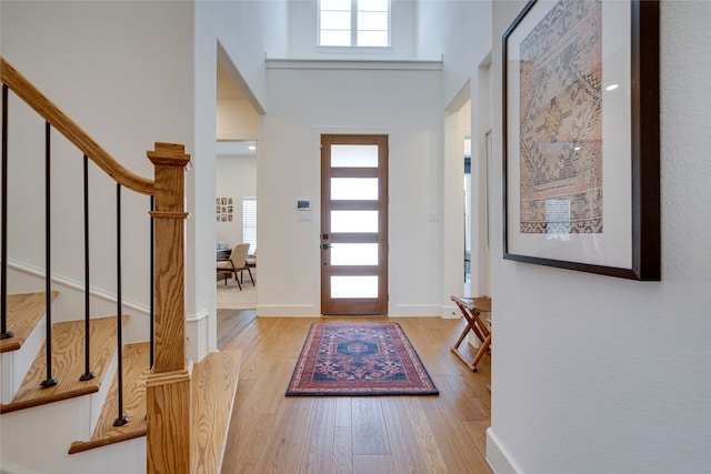 foyer with light hardwood / wood-style floors, a towering ceiling, and plenty of natural light