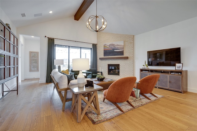 living room with an inviting chandelier, a brick fireplace, light hardwood / wood-style flooring, lofted ceiling with beams, and brick wall