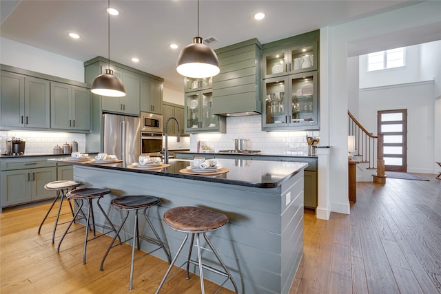 kitchen featuring a kitchen island with sink, tasteful backsplash, appliances with stainless steel finishes, and light hardwood / wood-style floors