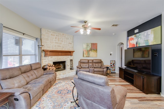 living room featuring light hardwood / wood-style flooring, ceiling fan, and a stone fireplace