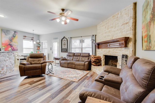 living room with ceiling fan, a stone fireplace, and light wood-type flooring